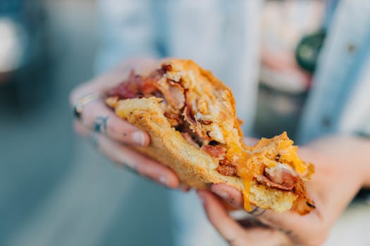 Delicious bacon egg sandwich with melted cheese in hand, perfect for food lovers.