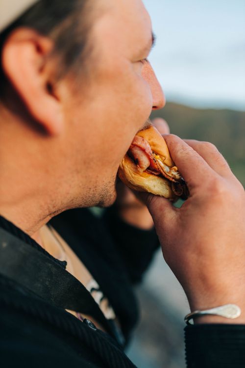 Free Close-up of a man eating a burger outdoors, capturing an authentic moment in natural light. Stock Photo