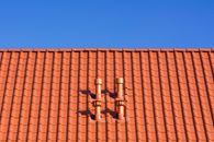 Vivid red clay rooftop with patterns and vents beneath a clear blue sky, ideal for architecture themes.