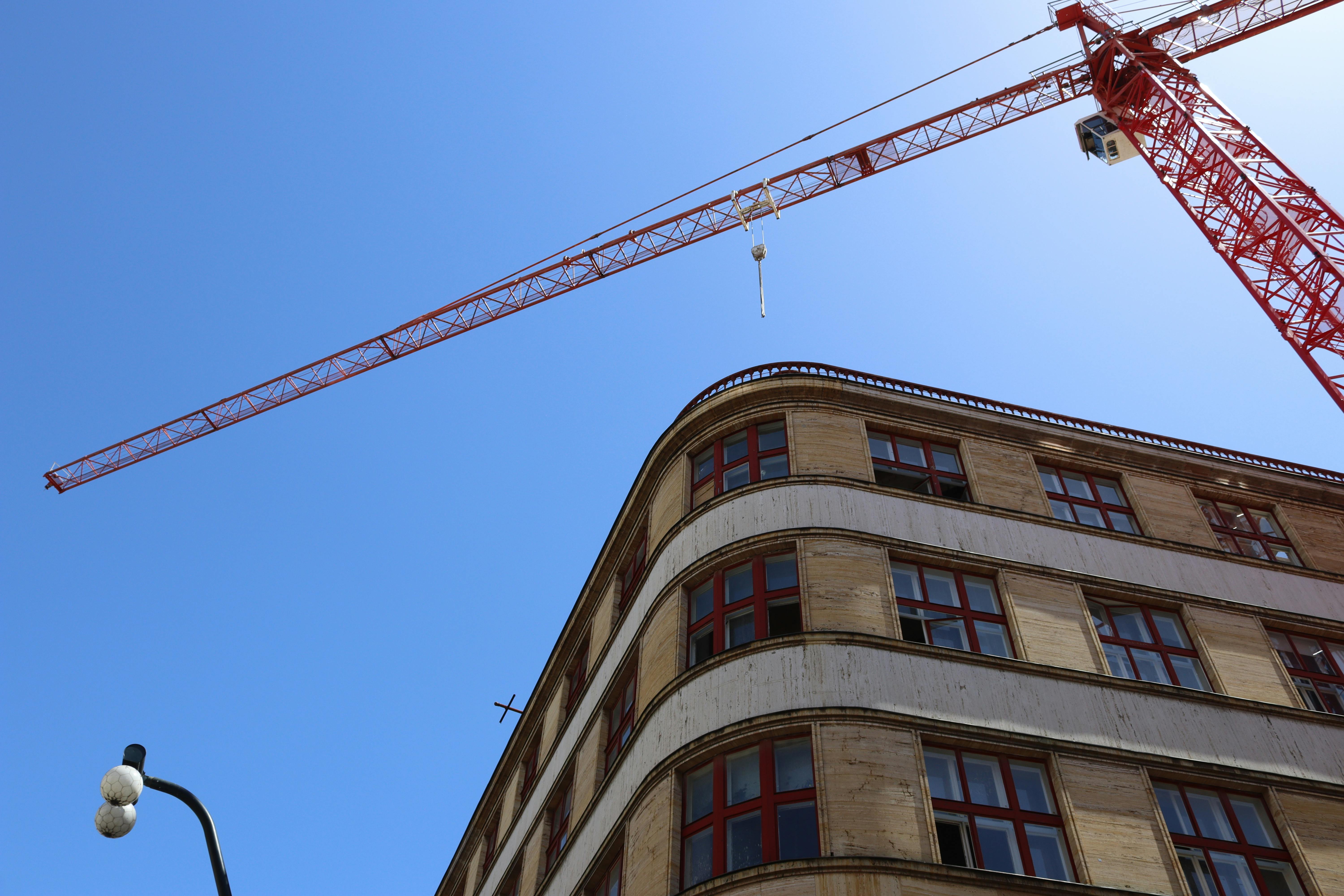 Free Low-angle view of a crane and building facade against a blue sky, perfect for construction themes. Stock Photo