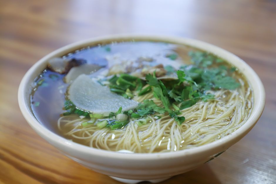 Warm noodle soup garnished with herbs and sliced radish in a ceramic bowl.