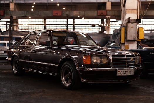 A classic black vintage car parked indoors in an industrial workshop setting with soft lighting.