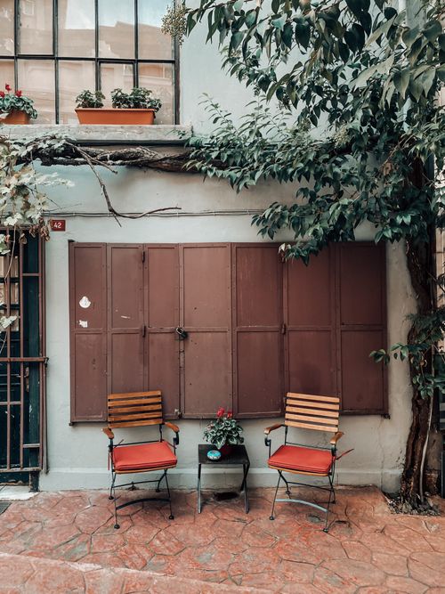 Free Two red-cushioned chairs on a rustic terrace with shutters and climbing plant. Stock Photo