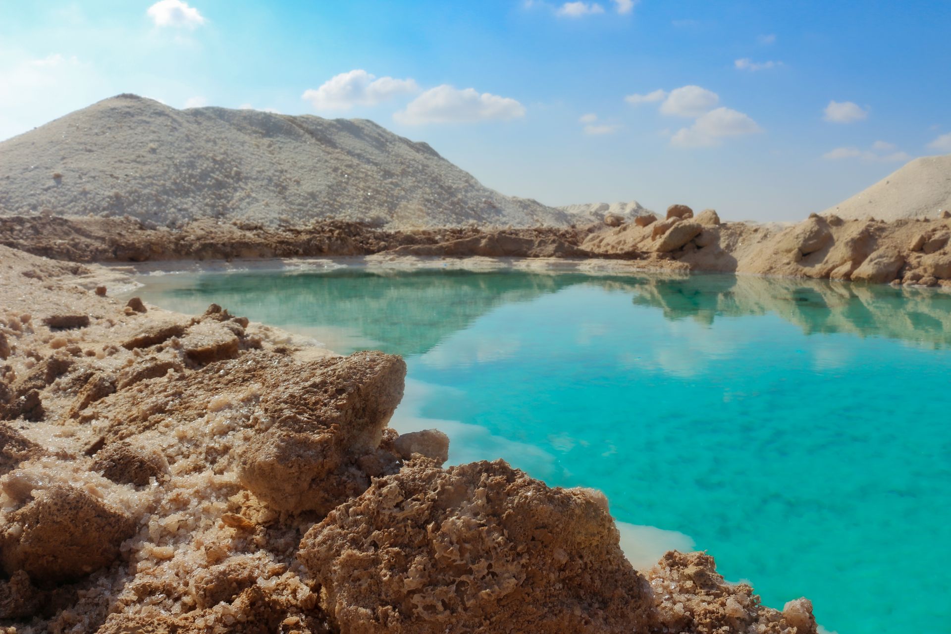 A tranquil turquoise lake surrounded by rugged rocky hills under a bright blue sky.
