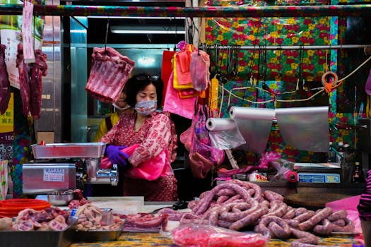 A female vendor in Taipei, Taiwan selling assorted meats at a colorful market stall.