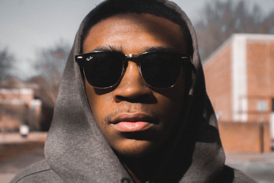 Portrait of a fashionable man wearing sunglasses and a hoodie outdoors in daylight.