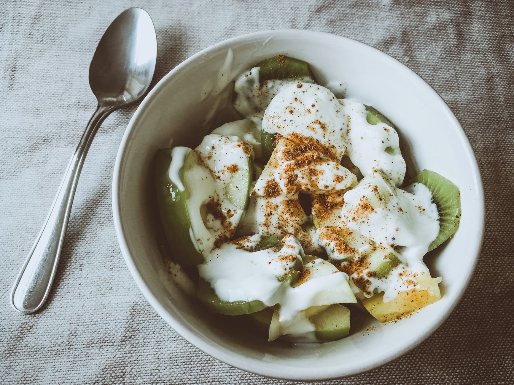 Fresh kiwi and pineapple slices topped with yogurt and cinnamon in a white bowl, perfect for a healthy breakfast.