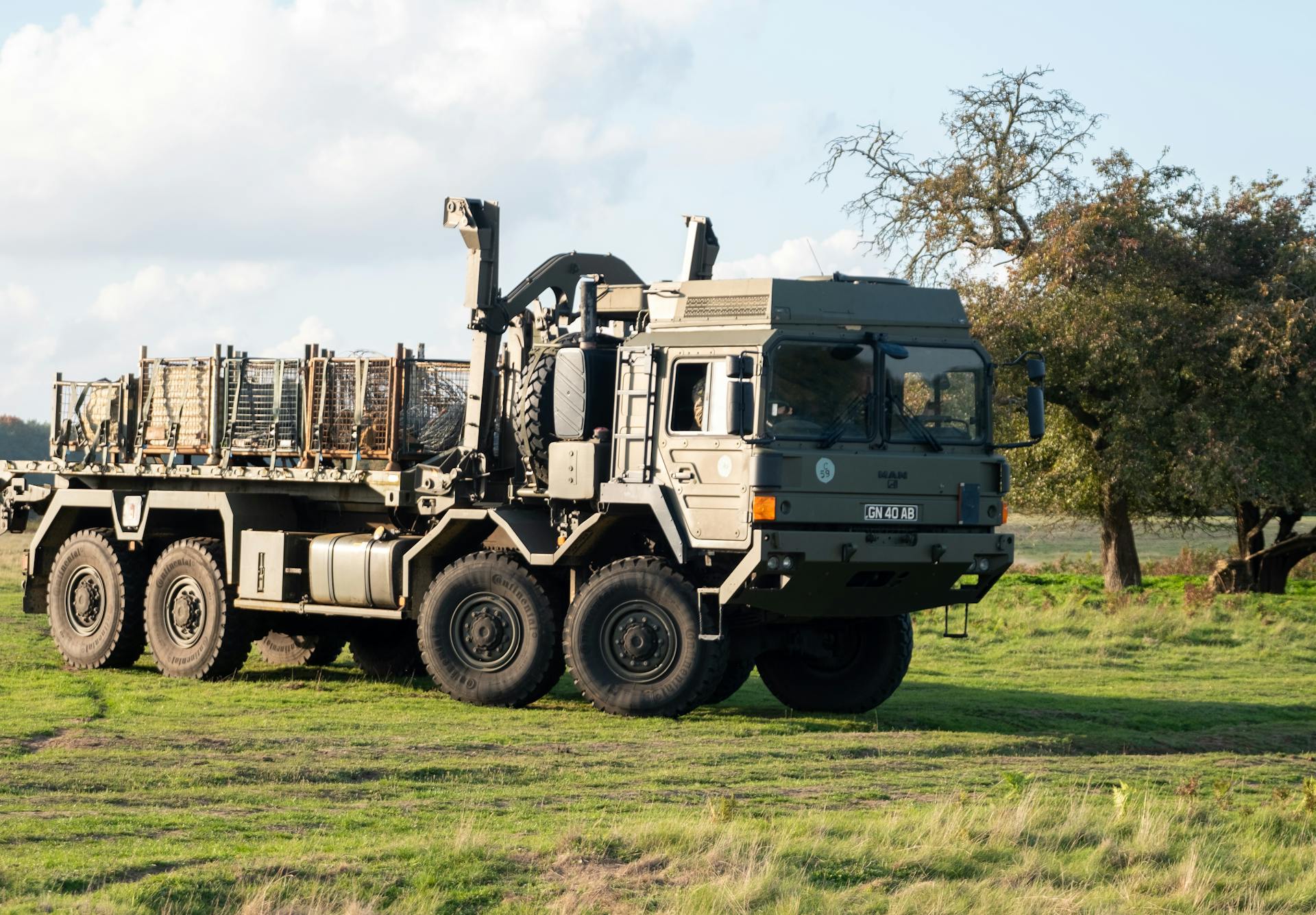 A military truck equipped with heavy machinery parked on a grass field under a cloudy sky.
