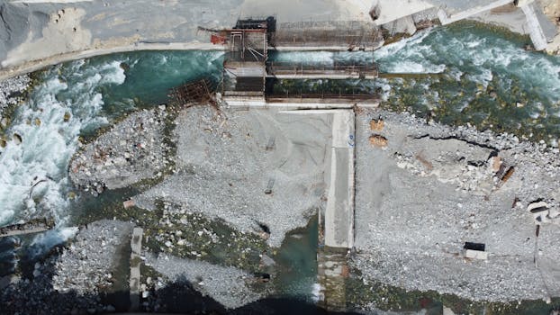 Aerial view of a construction site with a river in Matiltan, Pakistan, showcasing industrial development.