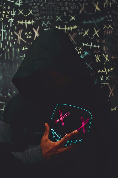 Free A hooded person wearing a neon mask stands against a chalk-marked wall, creating a mysterious vibe. Stock Photo