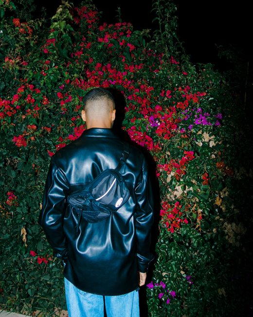 Man wearing a black leather jacket standing against a colorful garden backdrop at night.