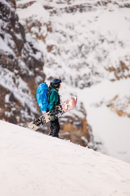 A snowboarder with gear traverses a snowy mountain slope in Banff, Canada, capturing the essence of winter adventure.