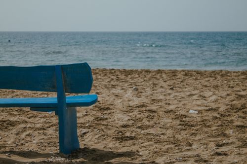 Free A serene beach scene with a blue wooden bench overlooking the ocean. Stock Photo