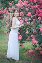一位美丽的女人穿着白色连衣裙，在宁静的公园里摆姿势，周围环绕着充满活力的粉红色花朵