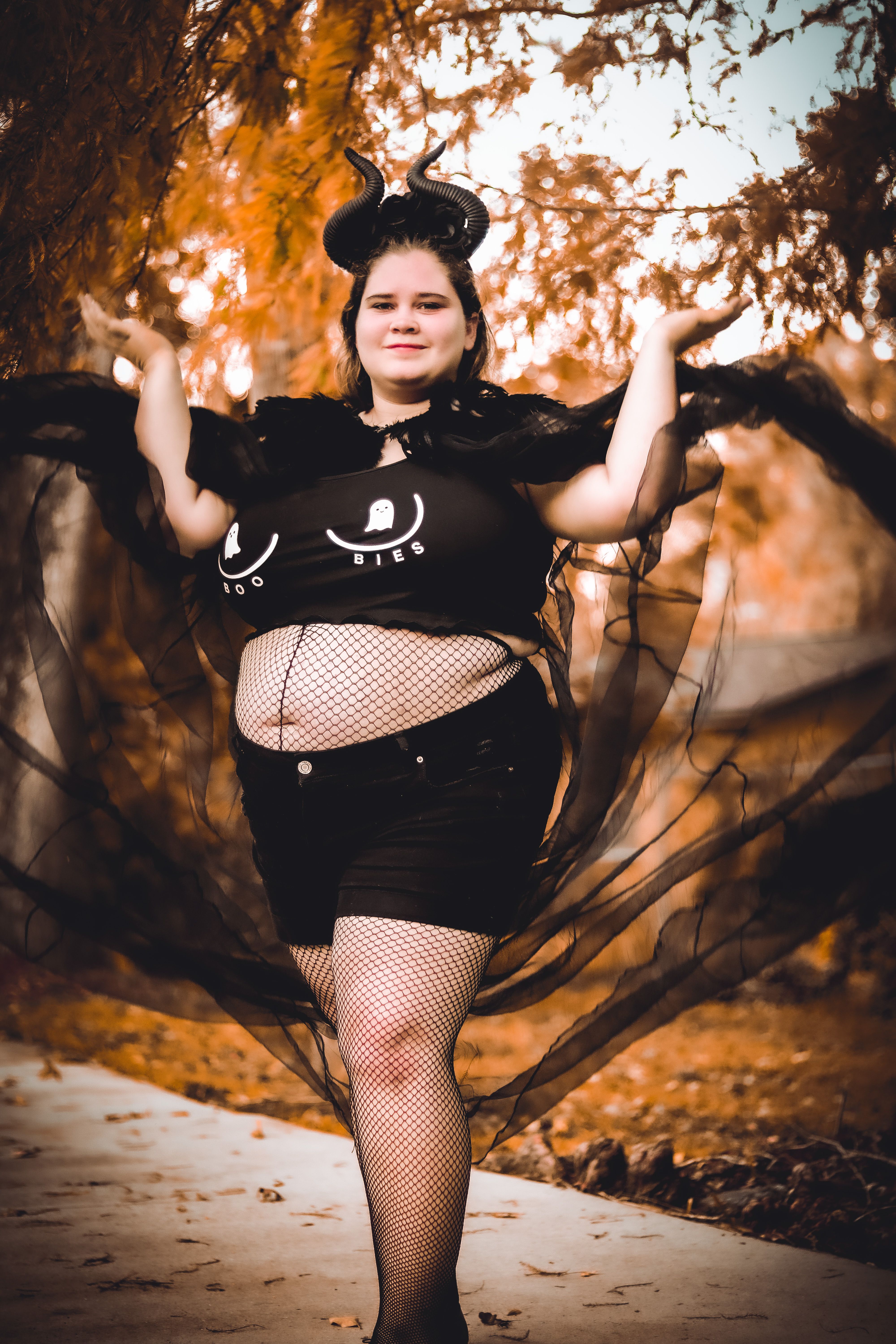 Woman in a Halloween costume posing outdoors with fall leaves and a smile.
