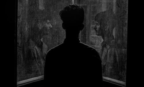 Free A contemplative scene of a man looking through a window with his reflection captured in black and white. Stock Photo