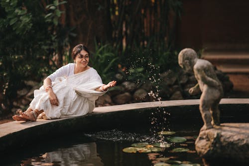 A Woman in White Dress Sitting Beside the Water Fountain