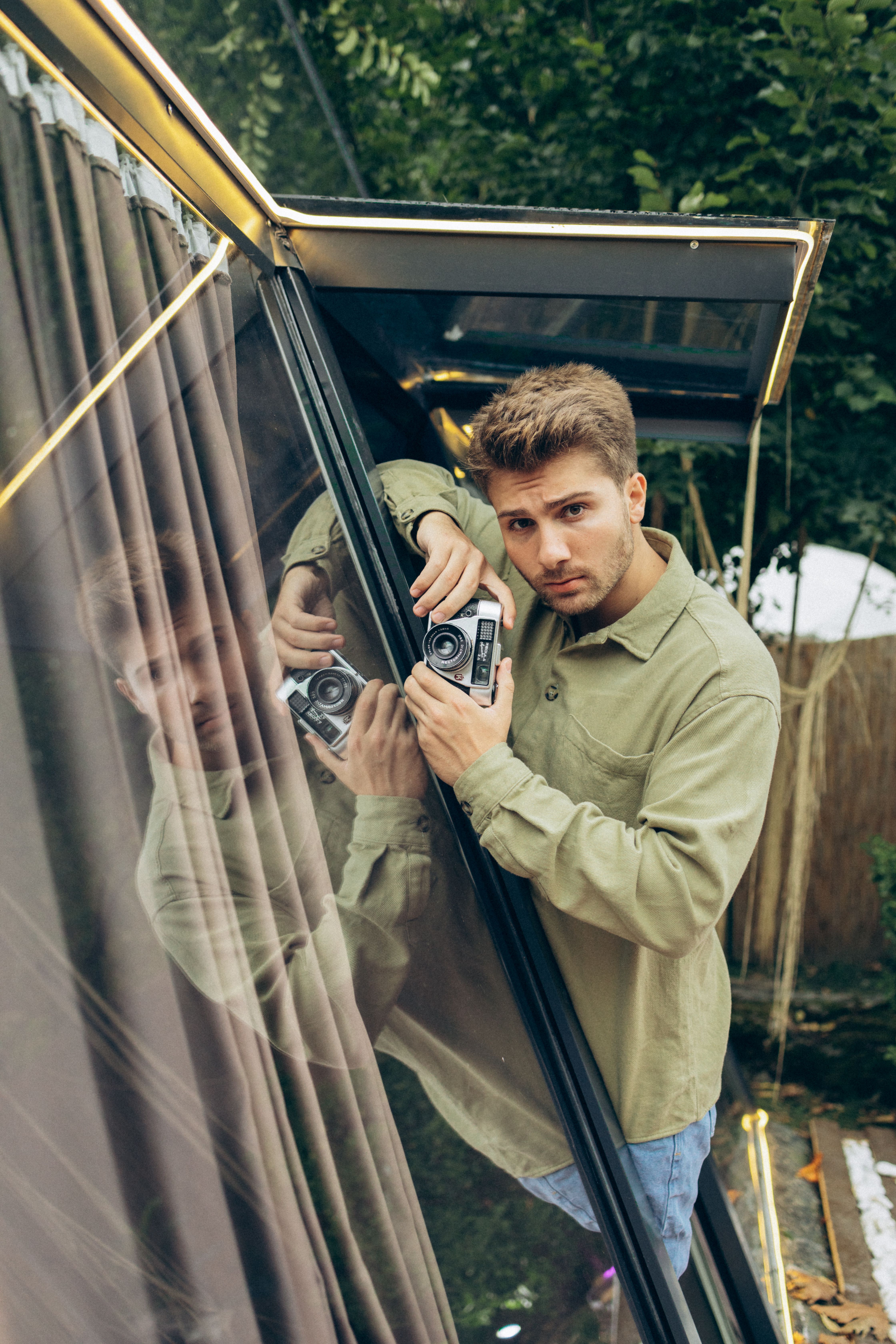 Portrait of a man in green shirt holding a camera, reflecting on glass in Sapanca, Turkey.