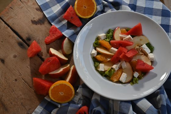 Salad of watermelon, orange segments, apple slices and feta cubes on greens in white bowl