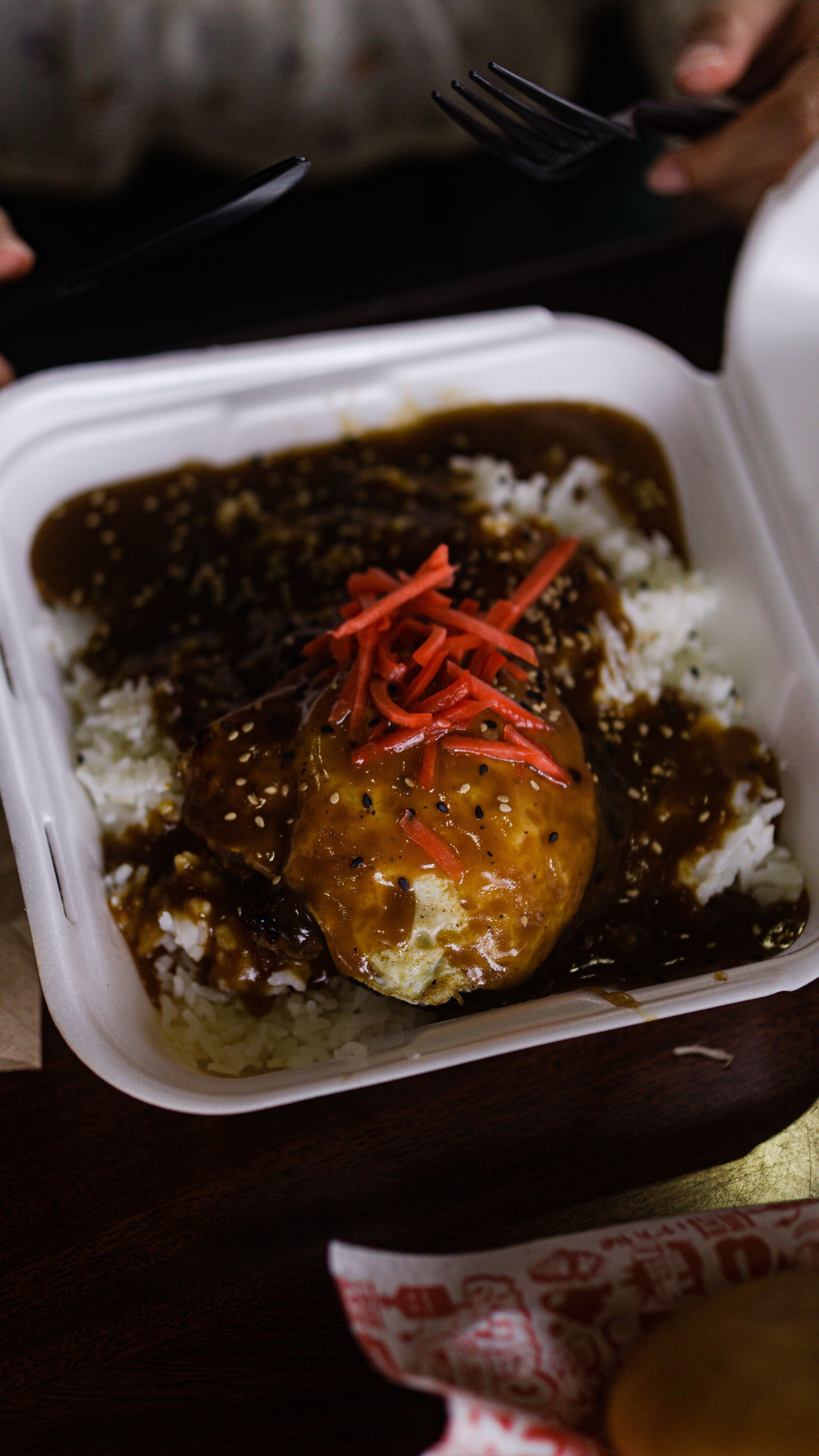 A white plate of loco moco showing a scoop of white rice topped with a seared hamburger patty, a fried egg with a runny yolk, and brown gravy pooling around the edges.