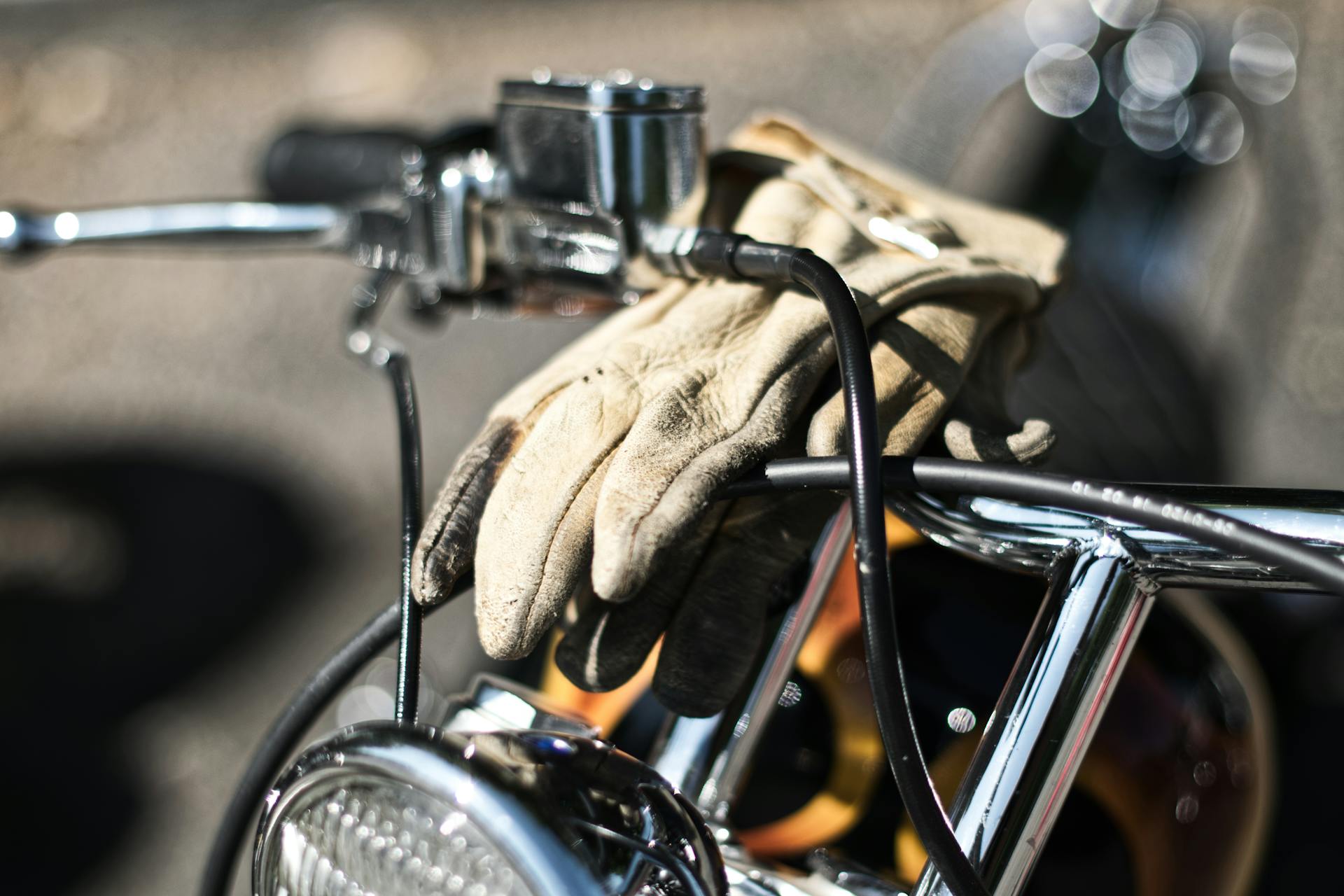 Vintage motorcycle handlebars with leather gloves draped over, highlighting classic chrome details.