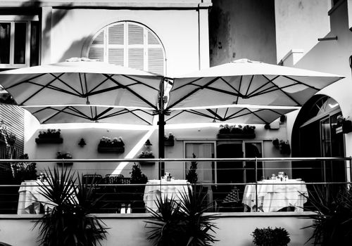 Free Charming black and white photo of an outdoor cafe in Antibes, France, featuring umbrellas and dining tables. Stock Photo
