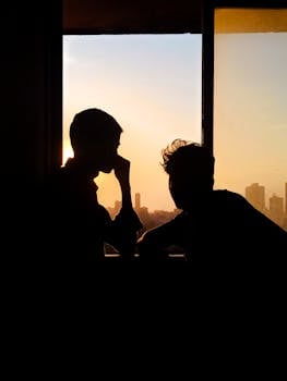 Silhouette of two people in an urban setting at sunset with a window view of Mumbai skyline.