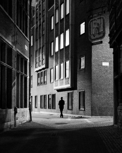 Free Monochrome image of a lone figure walking through urban streets at night. Stock Photo