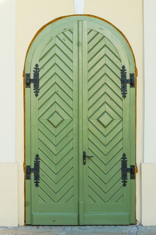 Free A tall, green, wooden door with intricate vintage-style black hinges on a pale wall. Stock Photo
