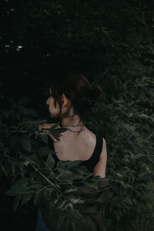 Free Back view of a woman surrounded by lush green leaves, creating a serene and natural atmosphere. Stock Photo