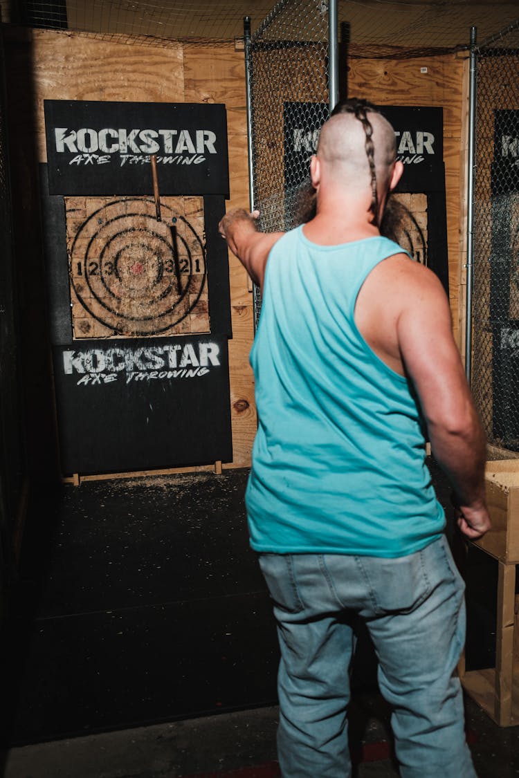 A Man In A Blue Tank Top Throwing An Axe