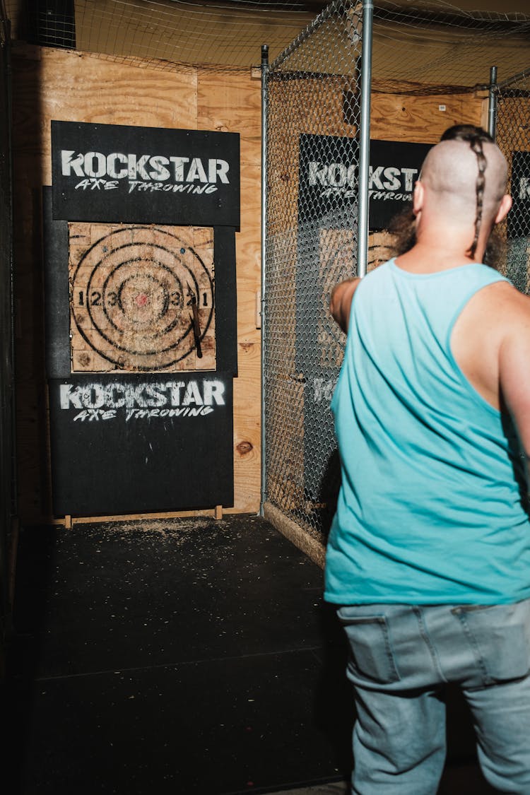 A Man In A Blue Tank Top Throwing An Axe