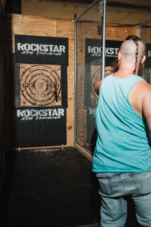 Free Adult man in blue tank top throwing an axe at an indoor target during daytime. Stock Photo