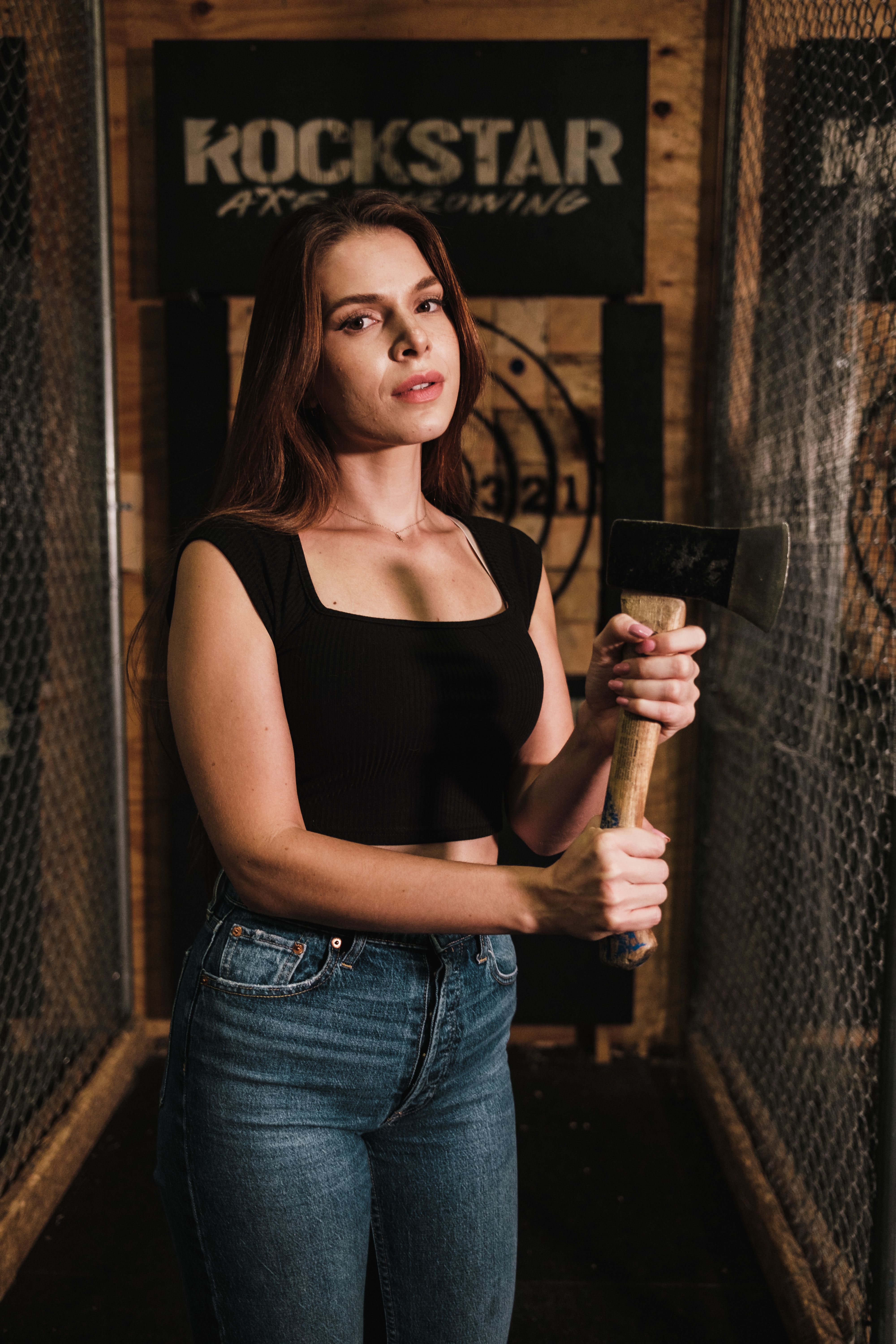 Confident woman in casual attire holding an axe at an indoor axe throwing venue.