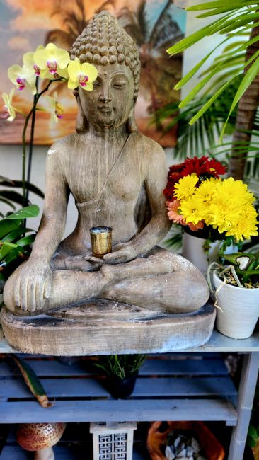 Serene wooden Buddha statue amidst colorful flowers on a shelf.