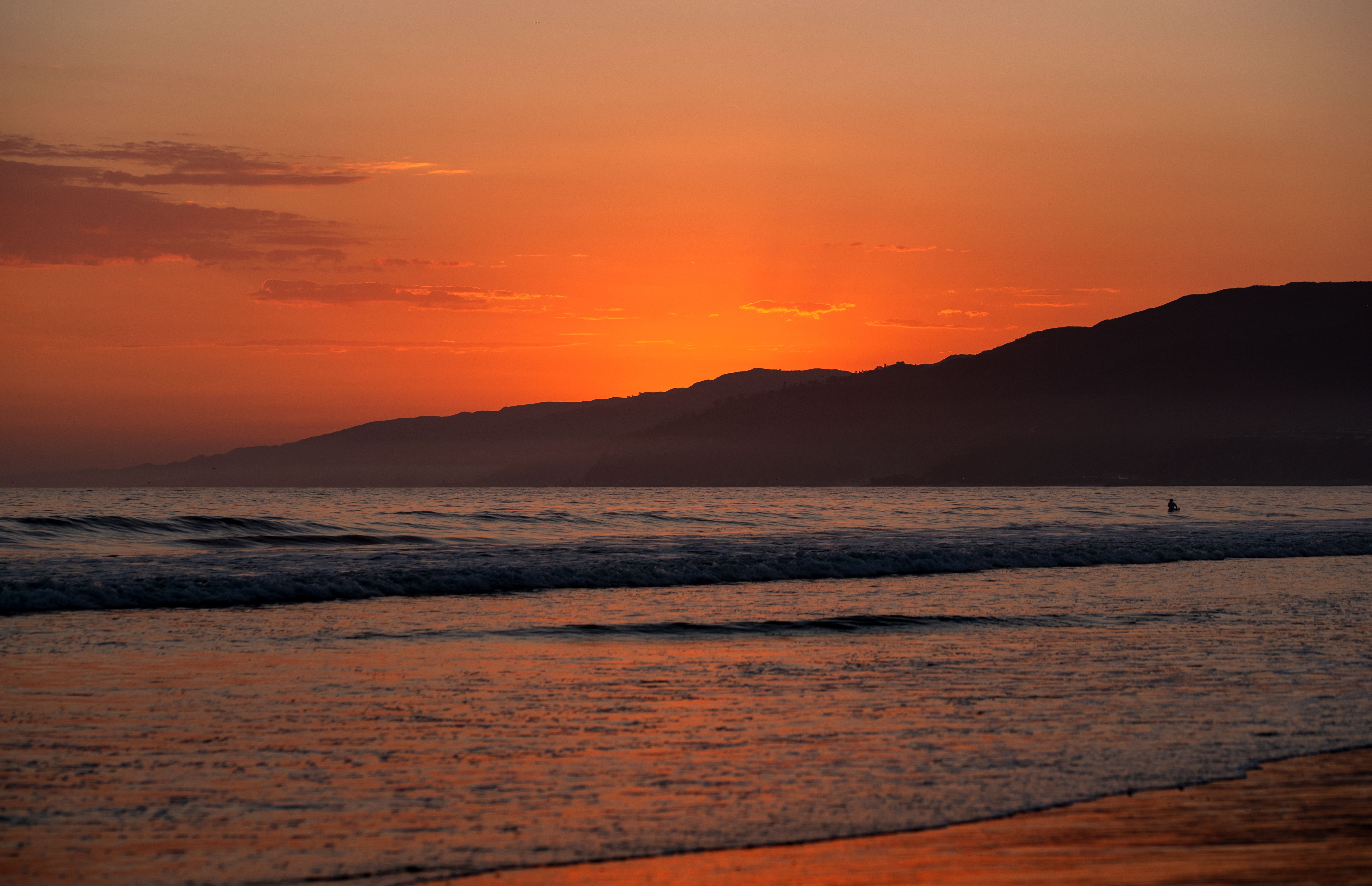 Beautiful sunset over the California coastline with waves and silhouette of mountains.