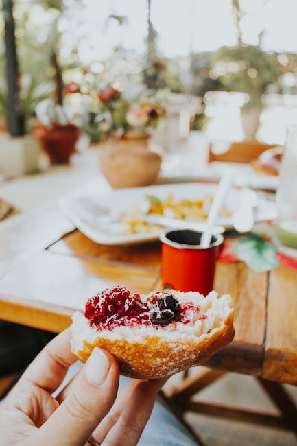 Close-up of a hand holding a brioche with jam, set on an outdoor breakfast table.