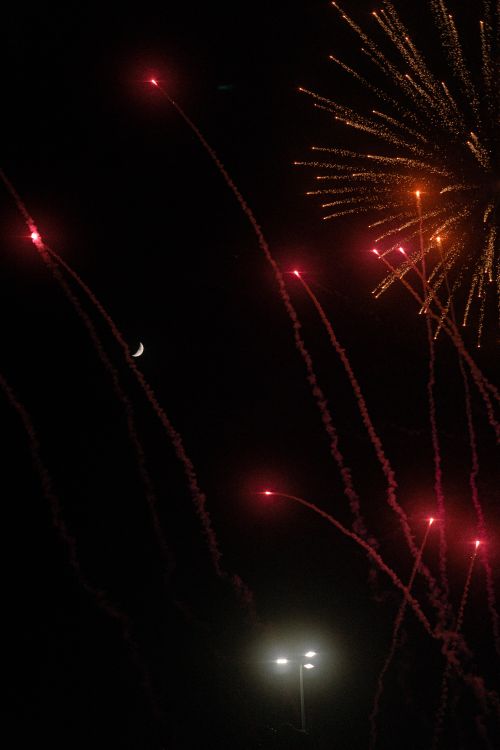 Free Dazzling fireworks lighting up a dark night sky with colorful sparks and a crescent moon visible. Stock Photo