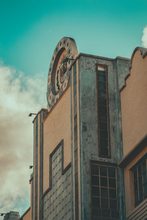 Free Vertical shot of an Art Deco building facade with decorative emblem under a blue sky. Stock Photo