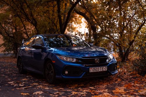 Free A shiny blue sedan parked on a tree-lined street surrounded by autumn leaves. Stock Photo