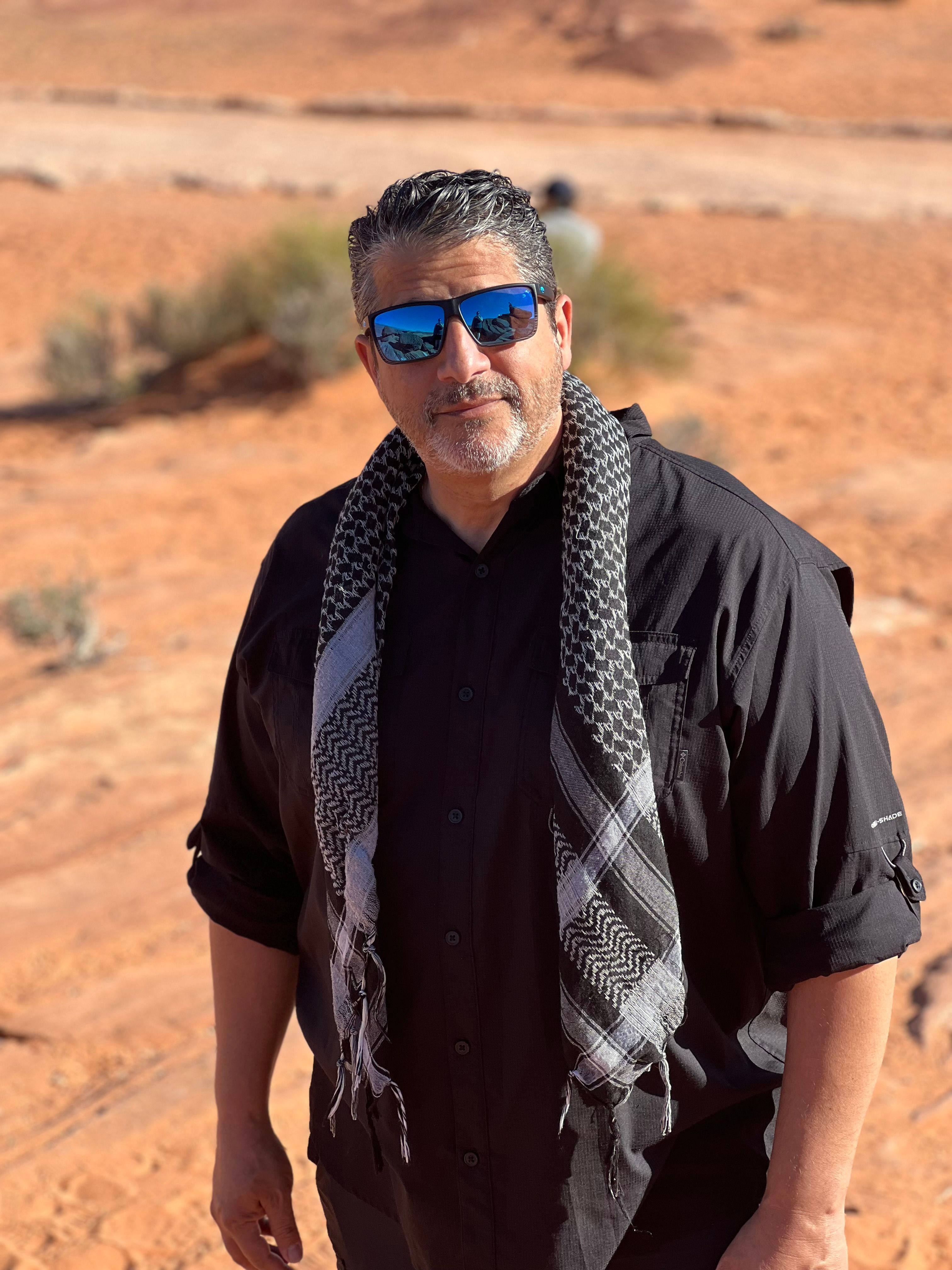 Caucasian man wearing a keffiyeh and sunglasses in the Arizona desert, embracing adventure.