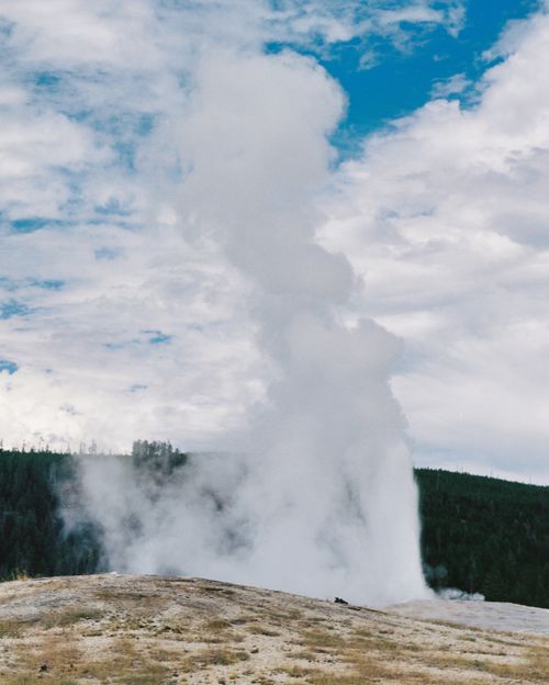 Free Captivating view of a geyser erupting amidst a cloudy sky and lush landscape, showcasing nature's power. Stock Photo
