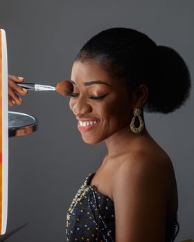 Beautiful woman with afro hair getting makeup applied in a studio setting, smiling.