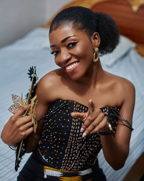 Free Cheerful woman in elegant attire smiling and holding a decorative fan in indoor setting. Stock Photo
