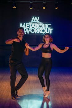 Dynamic duo performing energetic dance in a modern fitness studio with neon lights.
