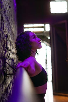 Artistic side view of a woman with curly hair, leaning against a textured wall under purple lighting.