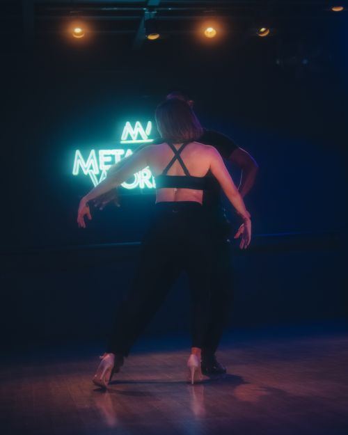 Free Couple dancing energetically in a dimly lit studio with a neon sign backdrop. Stock Photo