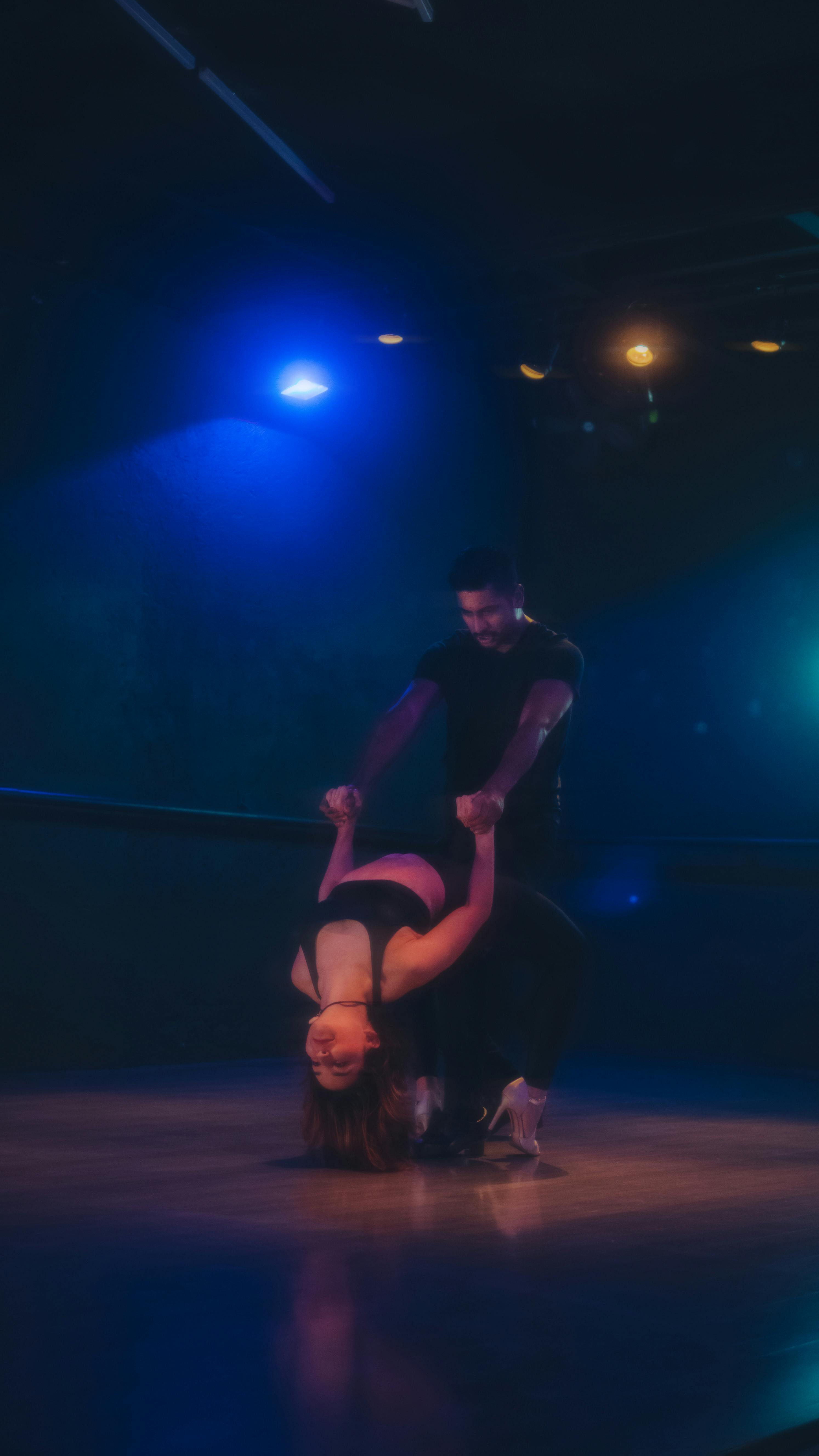 A couple performing a vibrant dance routine under dramatic stage lighting.