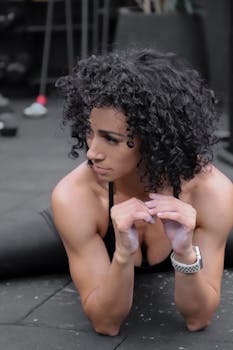 Fit woman with curly hair stretching on a gym floor, embodying fitness and wellness.
