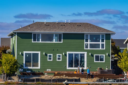 A modern green house under construction with blue skies and workers outside.